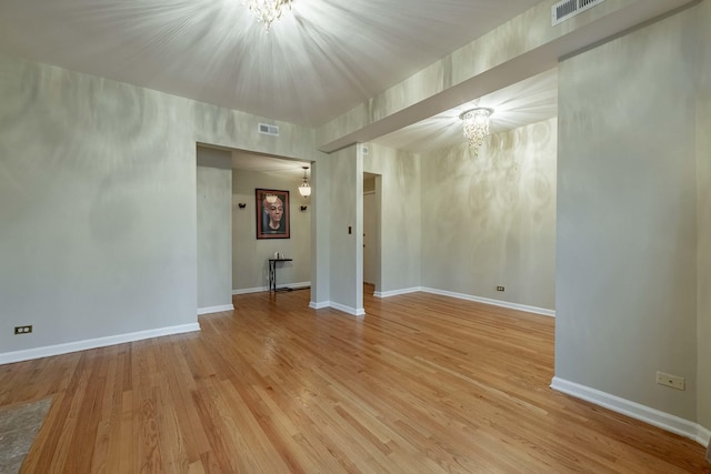 empty room featuring light wood-style floors, visible vents, baseboards, and an inviting chandelier