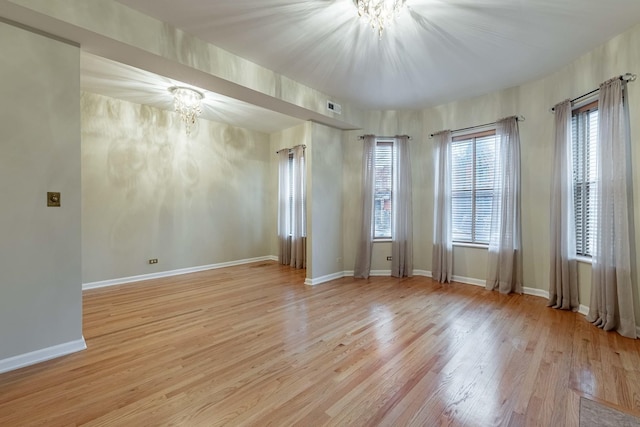 unfurnished room featuring baseboards, wood finished floors, visible vents, and a notable chandelier