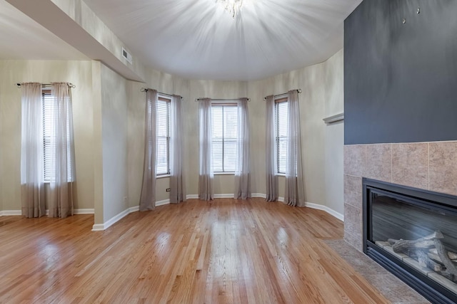 unfurnished living room featuring visible vents, baseboards, a tiled fireplace, and wood finished floors