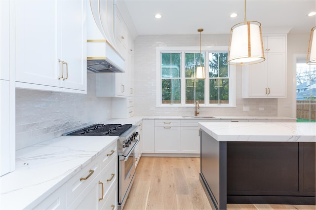 kitchen with high end stove, premium range hood, a sink, white cabinets, and light wood-type flooring