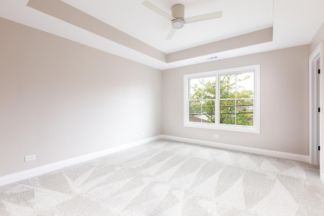 spare room featuring a tray ceiling, light colored carpet, and baseboards