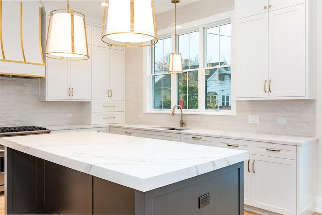 kitchen featuring a kitchen island, a sink, white cabinetry, wall chimney range hood, and gas stove