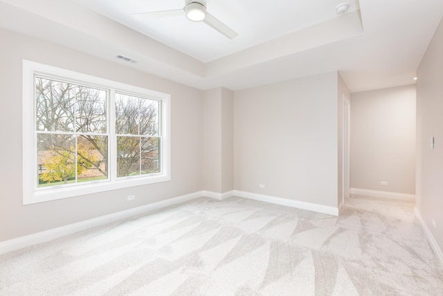 spare room with light carpet, visible vents, baseboards, a ceiling fan, and a tray ceiling