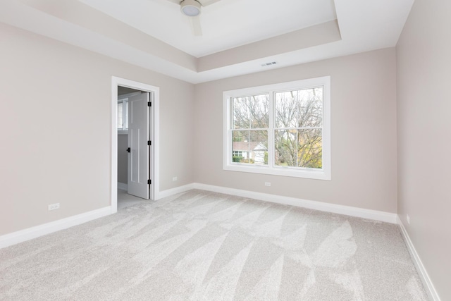 unfurnished room with light carpet, visible vents, baseboards, and a raised ceiling