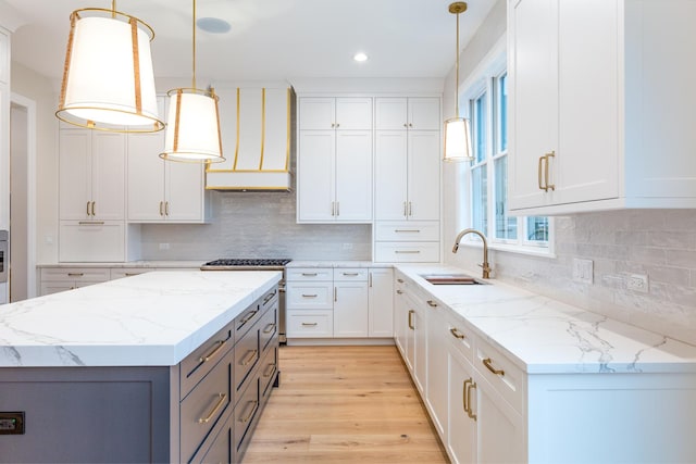 kitchen with light wood finished floors, white cabinets, hanging light fixtures, custom exhaust hood, and a sink