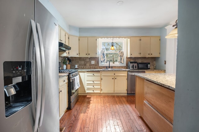 kitchen featuring under cabinet range hood, a sink, cream cabinetry, and appliances with stainless steel finishes