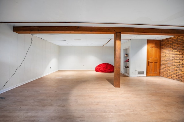 finished basement with visible vents, brick wall, and wood finished floors