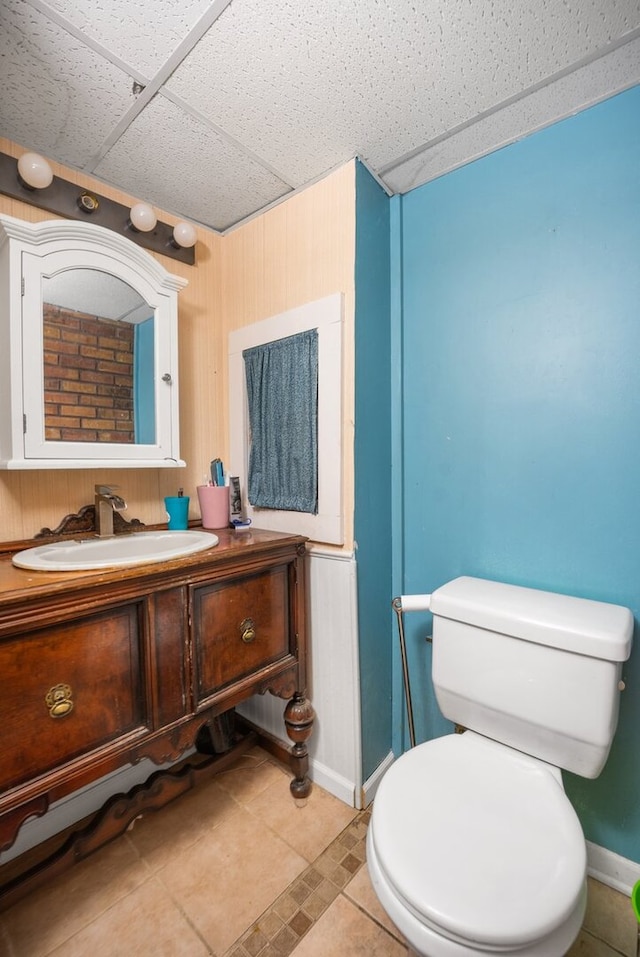 bathroom featuring tile patterned flooring, a drop ceiling, toilet, vanity, and baseboards
