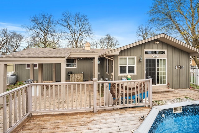 back of property with a wooden deck, a chimney, roof with shingles, and a swimming pool