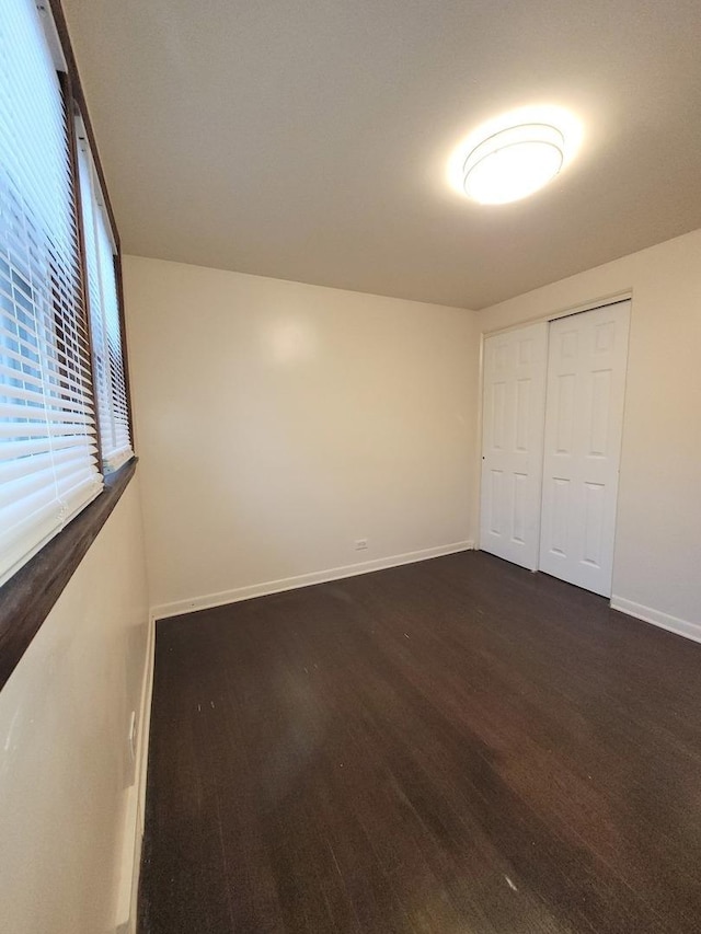 unfurnished bedroom featuring dark wood-style floors, a closet, and baseboards