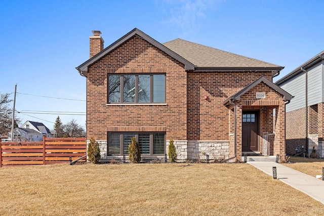 view of front facade with brick siding, fence, roof with shingles, a front lawn, and a chimney