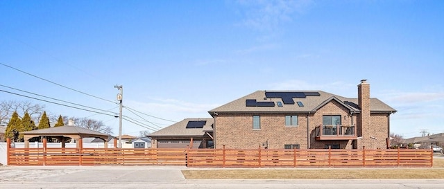 view of front of property with a fenced front yard, solar panels, brick siding, a gazebo, and a chimney