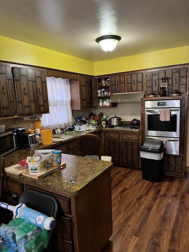 kitchen with dark brown cabinetry, stainless steel appliances, range hood, dark countertops, and dark wood finished floors