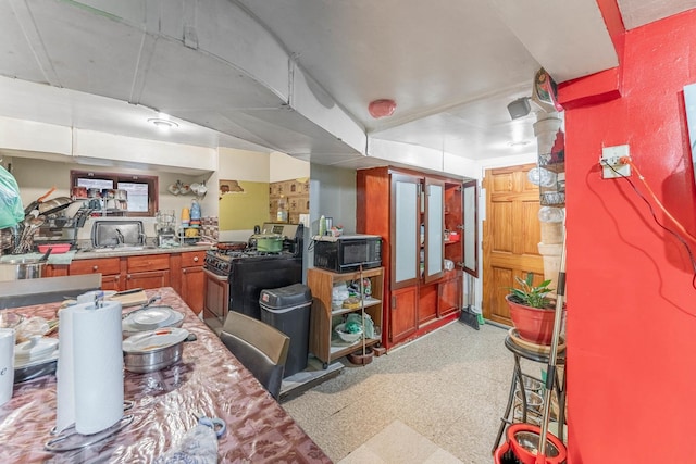 kitchen featuring black microwave, stainless steel gas range oven, a sink, light countertops, and light floors