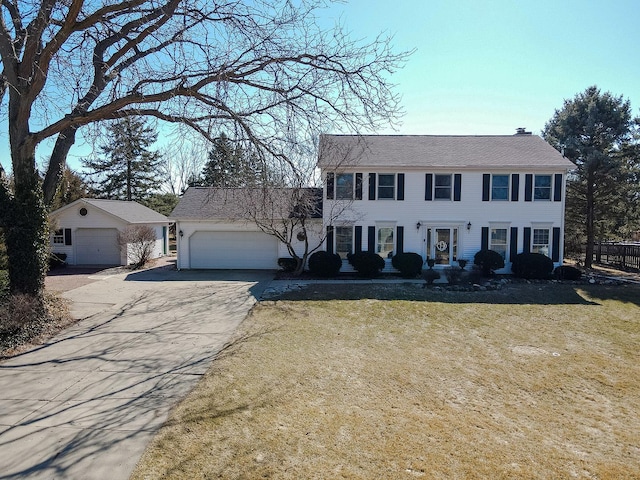 colonial home featuring a garage, driveway, a chimney, and a front lawn