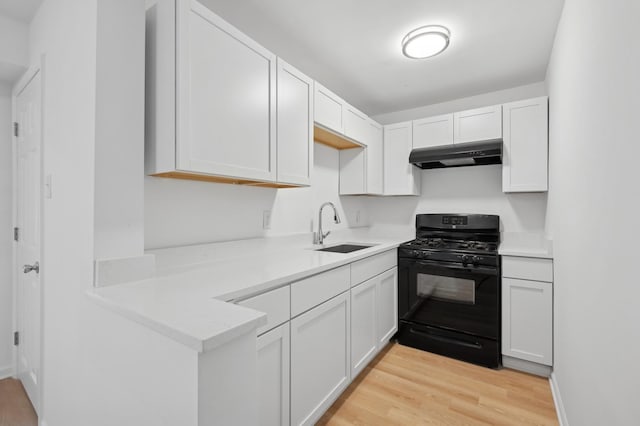 kitchen featuring light wood finished floors, light countertops, black gas range oven, a sink, and under cabinet range hood