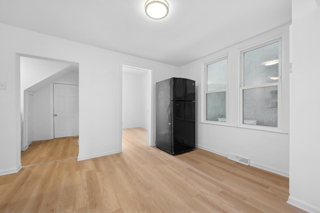 unfurnished bedroom featuring light wood-style floors, baseboards, visible vents, and freestanding refrigerator