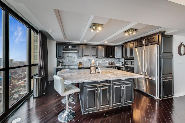 kitchen featuring stainless steel appliances, tasteful backsplash, dark wood finished floors, and light stone countertops