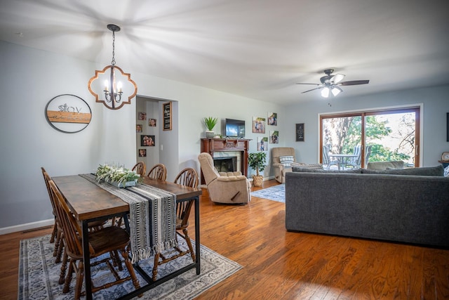 dining area featuring a fireplace, baseboards, wood finished floors, and ceiling fan with notable chandelier