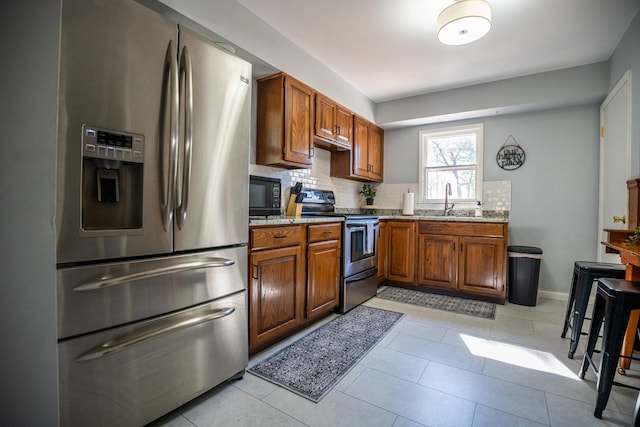 kitchen with brown cabinets, appliances with stainless steel finishes, decorative backsplash, and a sink