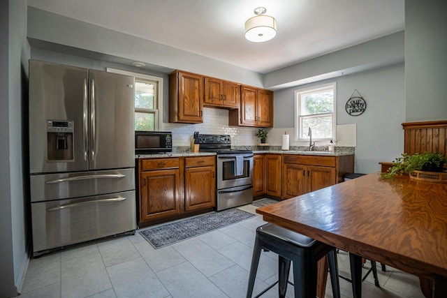 kitchen with light tile patterned flooring, a sink, appliances with stainless steel finishes, backsplash, and brown cabinets