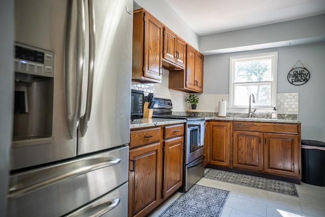 kitchen with light stone counters, stainless steel appliances, decorative backsplash, brown cabinetry, and a sink