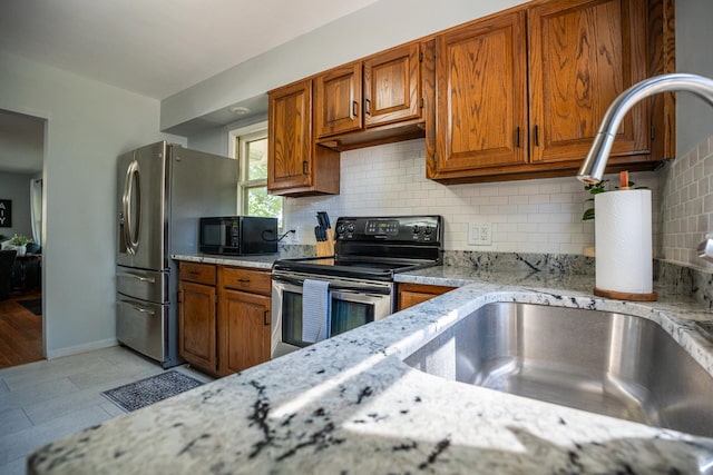 kitchen with light stone countertops, appliances with stainless steel finishes, brown cabinets, and backsplash