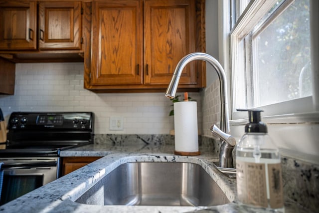 kitchen with brown cabinetry, decorative backsplash, light stone countertops, and stainless steel electric stove