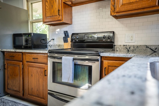 kitchen with black microwave, ventilation hood, backsplash, brown cabinets, and stainless steel electric range oven