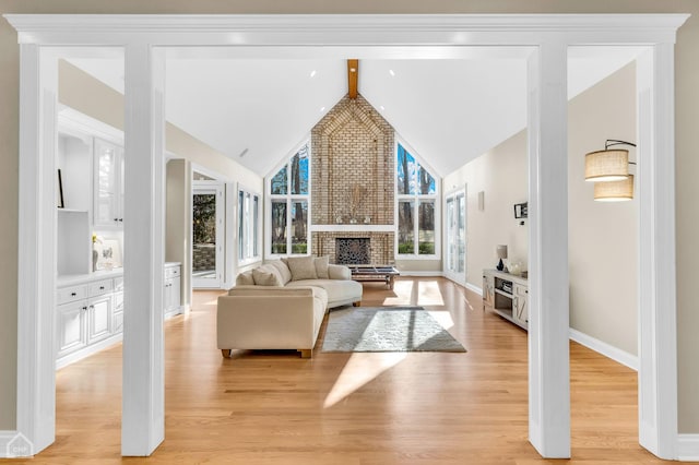 living area with light wood finished floors, baseboards, beamed ceiling, a brick fireplace, and high vaulted ceiling