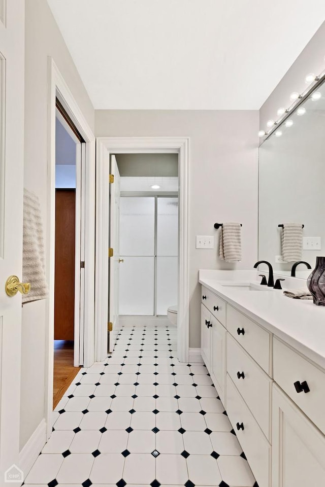 bathroom featuring toilet, baseboards, walk in shower, and vanity