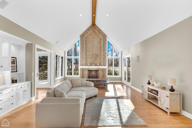 living area featuring high vaulted ceiling, light wood-type flooring, a fireplace, and beamed ceiling