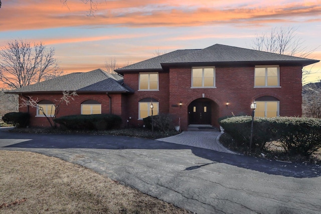 view of front of house with driveway, brick siding, and a shingled roof