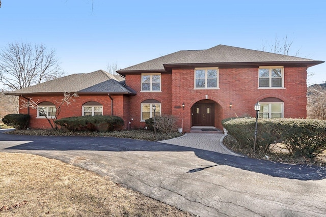 view of front of home featuring brick siding, driveway, and roof with shingles