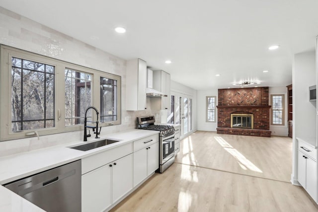 kitchen with a brick fireplace, light wood-style flooring, appliances with stainless steel finishes, and a sink