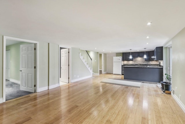 unfurnished living room featuring stairs, light wood-style flooring, and baseboards