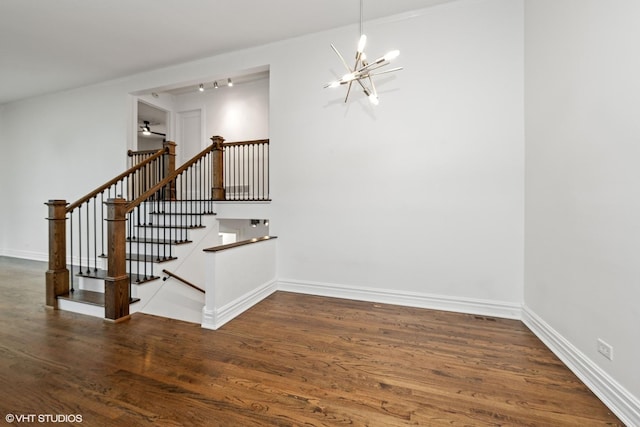 stairway featuring a chandelier, wood finished floors, rail lighting, and baseboards