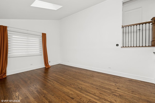 empty room with vaulted ceiling with skylight, wood finished floors, and baseboards