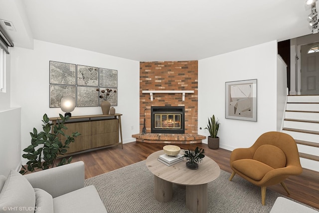 living area featuring a brick fireplace, visible vents, dark wood finished floors, and stairway