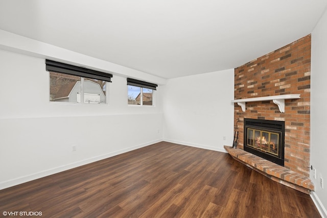 unfurnished living room with a brick fireplace, baseboards, and wood finished floors