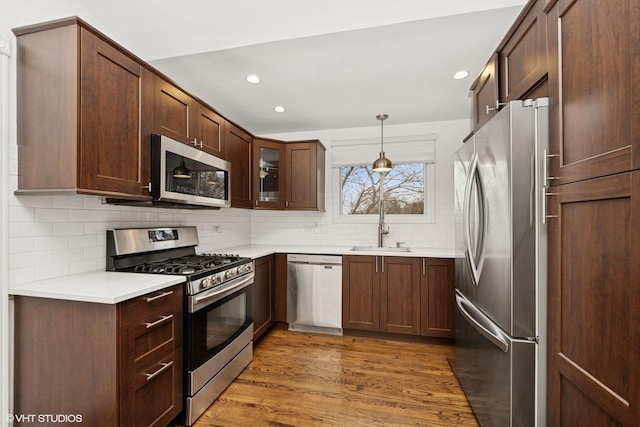 kitchen featuring light countertops, backsplash, appliances with stainless steel finishes, a sink, and wood finished floors