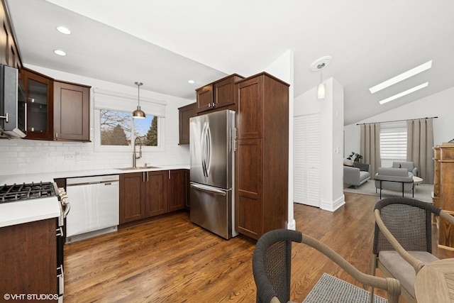 kitchen with dark wood finished floors, freestanding refrigerator, white dishwasher, a sink, and vaulted ceiling with skylight