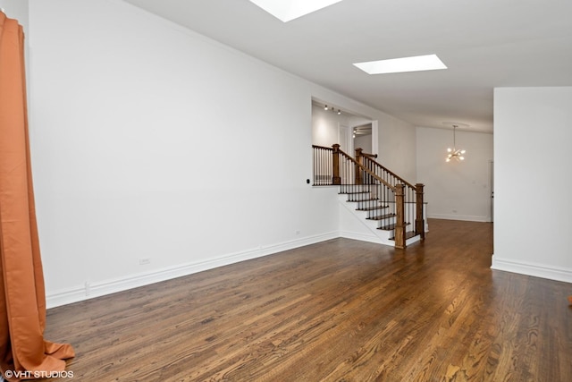 empty room featuring baseboards, lofted ceiling with skylight, stairway, dark wood-type flooring, and a chandelier