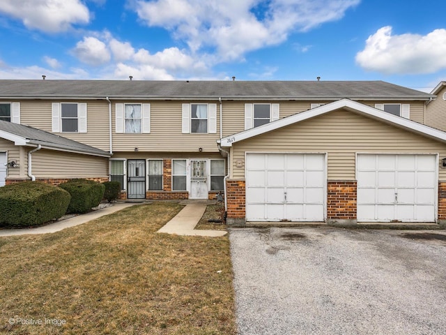 view of property with brick siding, an attached garage, driveway, and a front lawn