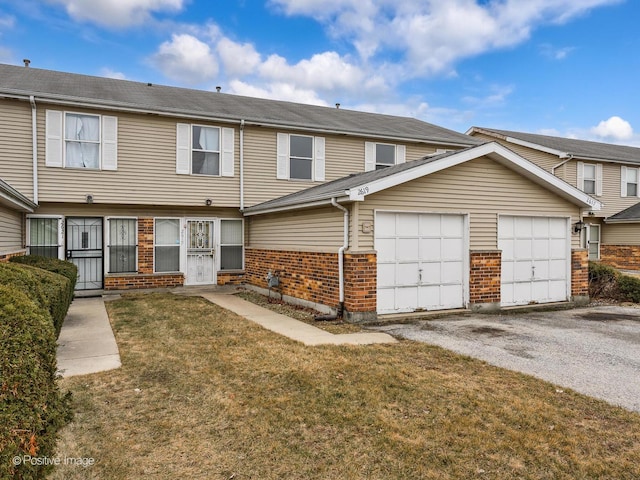 townhome / multi-family property featuring brick siding, driveway, a front yard, and a garage