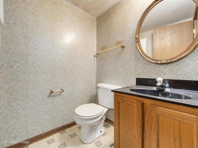 bathroom featuring vanity, toilet, baseboards, and wallpapered walls