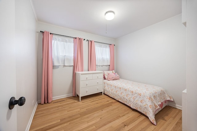 bedroom with crown molding, light wood finished floors, visible vents, and baseboards