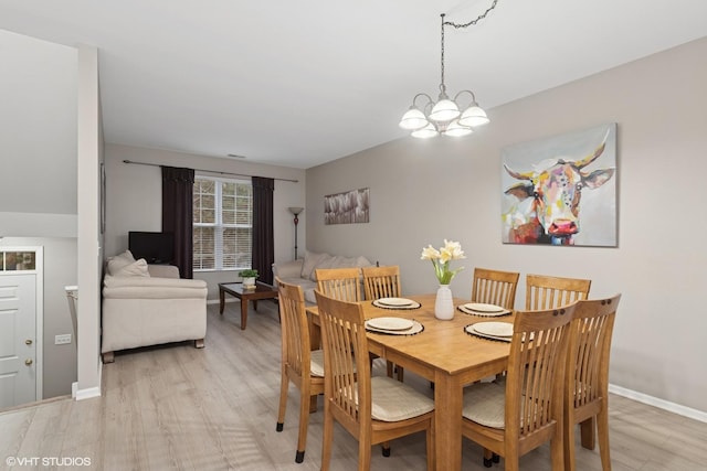 dining space with light wood-type flooring, a notable chandelier, and baseboards