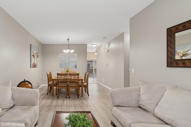 living area with light wood-type flooring, baseboards, and an inviting chandelier