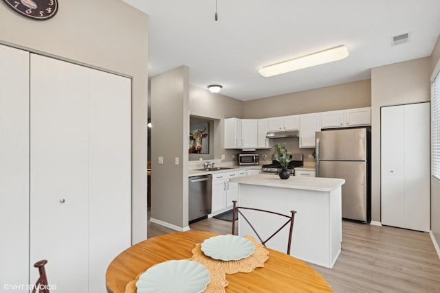 kitchen featuring light countertops, appliances with stainless steel finishes, white cabinetry, a sink, and under cabinet range hood